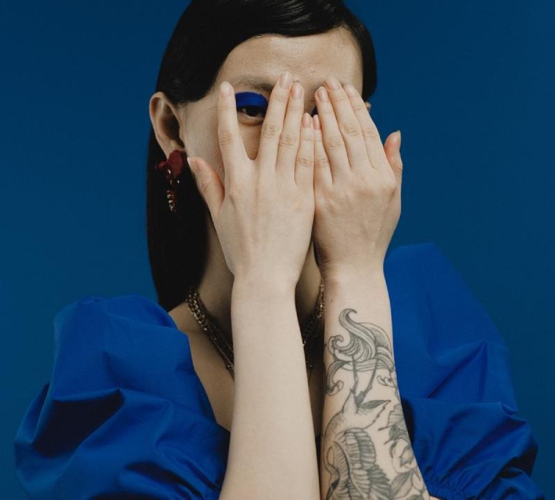 A woman with tatoos on her hand hiding her face with her palms and still peeking through the fingers seeing the new world